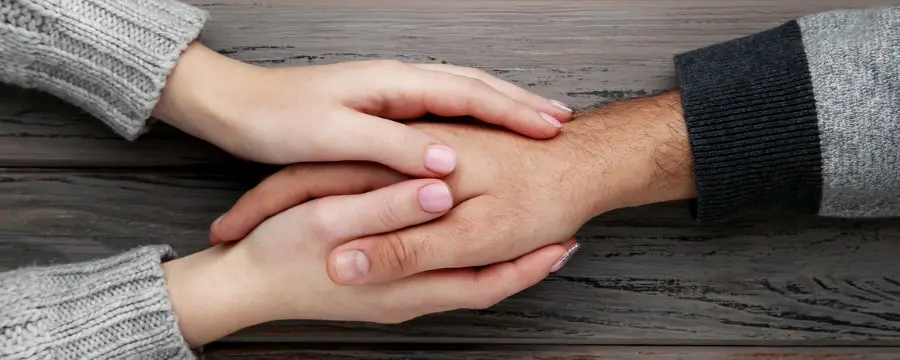 One hand being held by two hands to represent the support of a counselor providing cognitive behavioral therapy