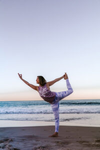 Side view of woman on beach leaning forward doing Yoga.