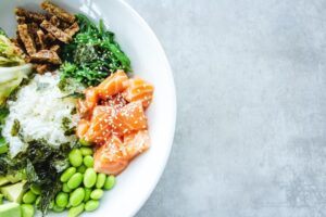 Bowl of food containing rice, salmon, green vegetables, and grains.