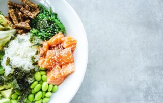 Bowl of food containing rice, salmon, green vegetables, and grains.