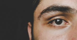 A quarter of man’s face, with eye taking up half the frame on a black background.