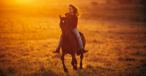 A woman riding on a horse through a field for an equine therapy session.